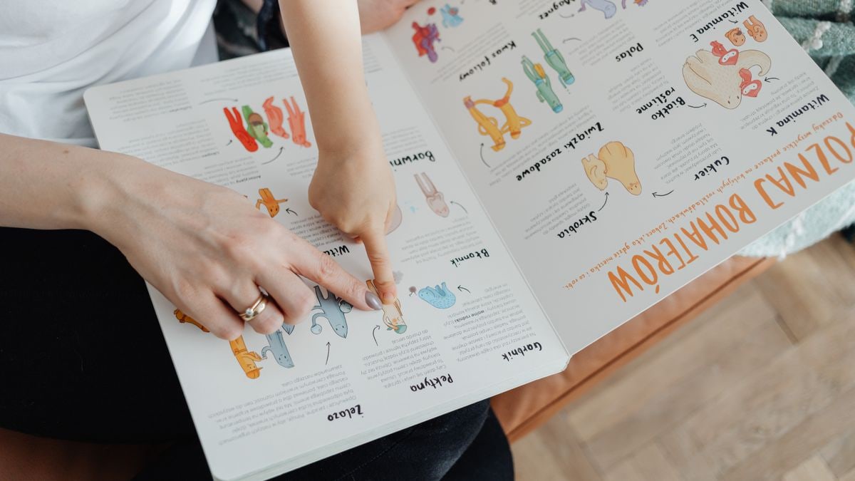A child and adult engaging with an educational book, pointing to illustrations.